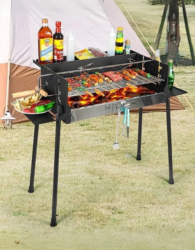 A large charcoal BBQ grill with offset smoker, set up outdoors with bottles and food on the side, indicating it is in use or has been used recently.